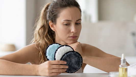 Femme hesitante en regardant les trois cotons démaquillants réutilisables en microfibre qu'elle tient en main dans une salle de bain.